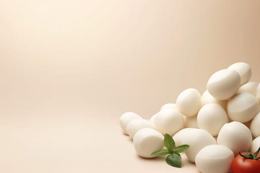 Fresh mozzarella balls with basil and a tomato on a beige background.