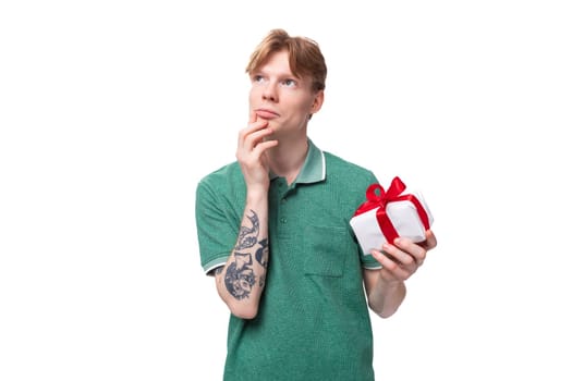 a young man with red hair dressed in a green T-shirt is dreaming about the holiday holding a gift.