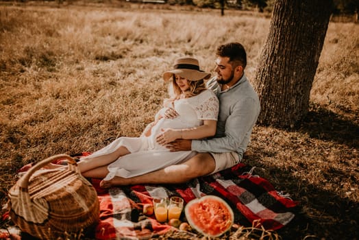 happy European caucasian family with a pregnant woman relaxing in nature picnic hug laugh having fun. expectant mother in hat and dress in summer. face with moles