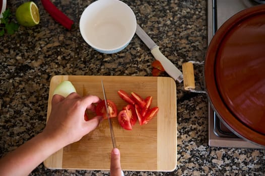 Close-up view from above of a cook chef, using kitchen knife slicing chopping cutting tomatoes on a wooden board. Food background