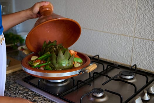 Closeup of a housewife cooking vegetables in tagine clay dish at home kitchen. The concept of traditional and national Moroccan food