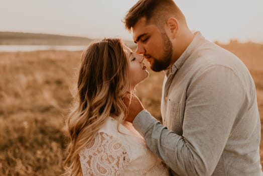 husband kisses his wife holding his hand on her cheek. Happy family resting in nature hugs kisses in summer at sunset. future mother Caucasian pregnant woman in white cotton dress. father