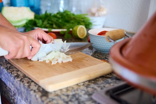 Close-up housewife's hands using kitchen knife, slicing and chopping onion on wooden cutting board, preparing a healthy salad for dinner at home. Healthy eating concept. Food background. Culinary