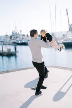 Smiling dad spins a little girl in his arms on the pier. Back view. High quality photo
