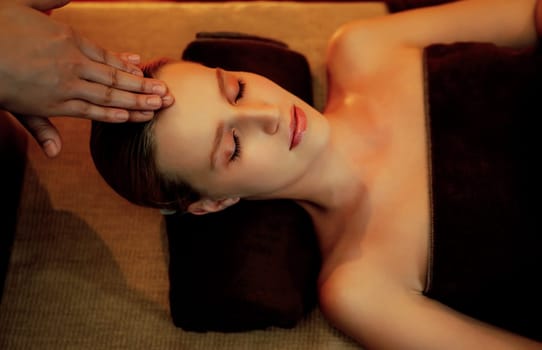 Caucasian woman enjoying relaxing anti-stress head massage and pampering facial beauty skin recreation leisure in warm candle lighting ambient salon spa in luxury resort or hotel. Quiescent