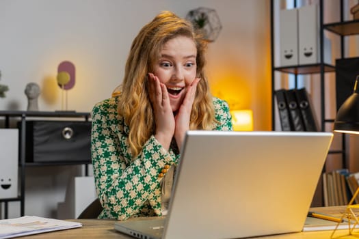 Oh my God, wow. Happy amazed blonde Caucasian businesswoman working on laptop shocked by sudden victory, game winning, lottery goal achievement, good news. Girl woman freelancer at home office desk.