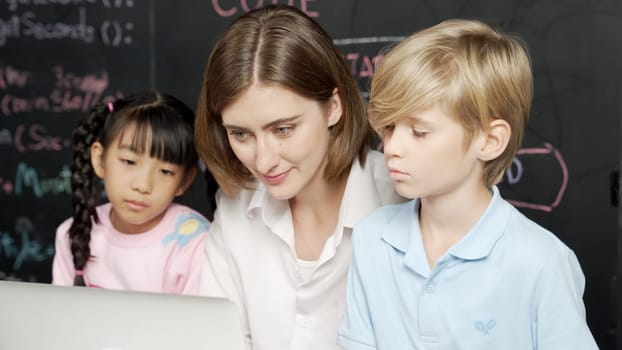 Young smart teacher using laptop to teach diverse student programing system. Caucasian learner looking at computer screen while study about coding prompt at blackboard with program code. Erudition.