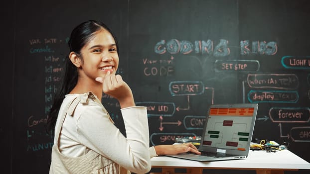 Smart girl using laptop coding or programing system at blackboard. Happy highschool student working on laptop while showing miniheart and looking at camera at STEM technology class. Edification.