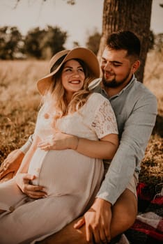 happy European caucasian family with a pregnant woman relaxing in nature picnic hug laugh having fun. expectant mother in hat and dress in summer. face with moles