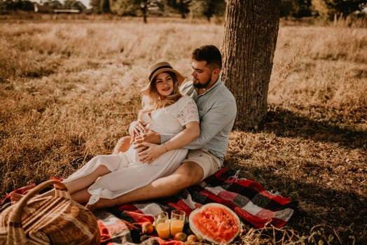happy European caucasian family with a pregnant woman relaxing in nature picnic hug laugh having fun. expectant mother in hat and dress in summer. face with moles