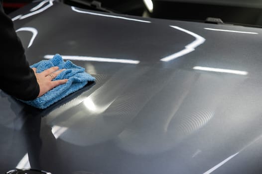A man wipes the surface of the body of a gray car with a microfiber cloth