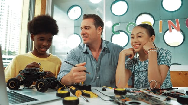 Caucasian student asking teacher about code and pointing at laptop screen. Professional instructor answer girl question while boy repair car model at table with electronic tool placed. Edification.