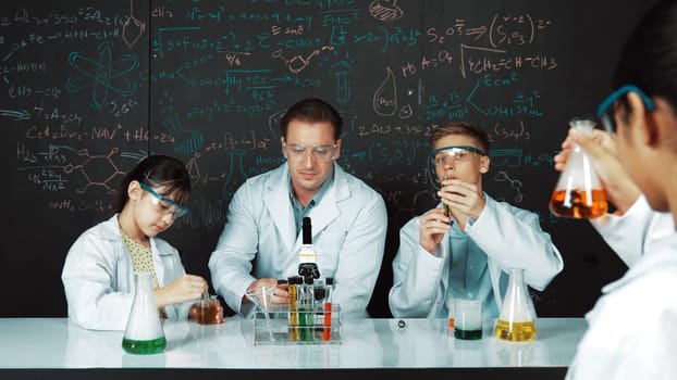 Smart teacher explain about chemical theory while student mixing colored solution or doing experiment. Instructor teaching chemistry while pointing at blackboard in STEM science class. Edification.