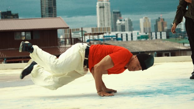 Caucasian hipster doing freeze pose in B-boy performance at roof top of high building. Young professional man break dancing at rooftop with city or urban view background. Outdoor sport 2024. Endeavor.