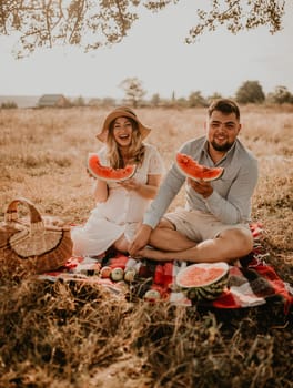 happy European caucasian family with a pregnant woman relaxing in nature picnic eating fruit red juicy watermelon laugh having fun. expectant mother in hat and dress eating watermelon in summer.