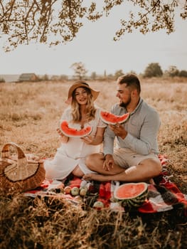 happy European caucasian family with a pregnant woman relaxing in nature picnic eating fruit red juicy watermelon laugh having fun. expectant mother in hat and dress eating watermelon in summer.