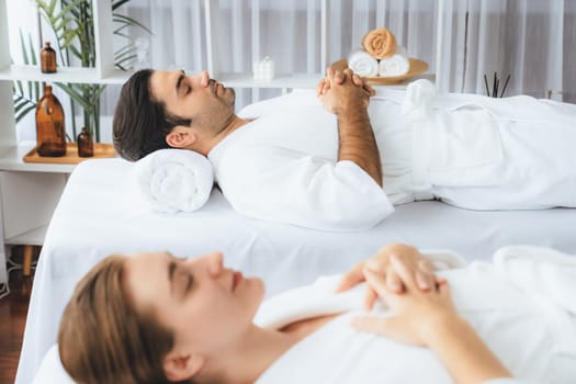 Caucasian couple customer enjoying relaxing anti-stress spa massage and pampering with beauty skin recreation leisure in day light ambient salon spa at luxury resort or hotel. Quiescent