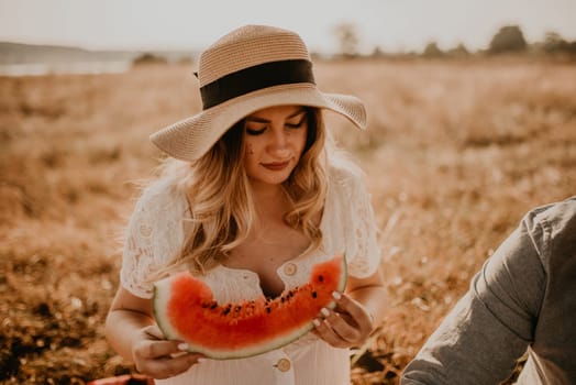 happy European caucasian pregnant woman relaxing in nature picnic eating fruit red juicy watermelon laugh having fun. expectant mother in hat and dress eating watermelon in summer. face with moles