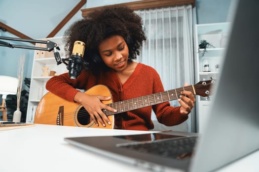 Host channel in musician of young African American playing guitar along with singing, broadcasting on laptop in studio. Decoration of equipment of headsets and recording microphone. Tastemaker.