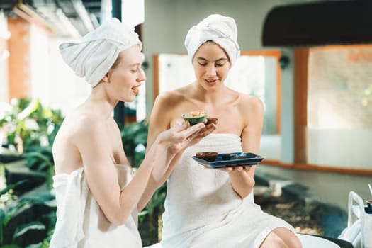 Couple of beautiful woman interested in homemade facial masks while sitting at spa salon. Attractive woman in white towel enjoy herbal masks with her friend surrounded by nature. Tranquility.