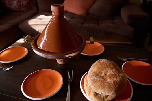 Traditional Moroccan tasty meal cooked in tagine clay pot with freshly baked bread on the table at home. Cultures, traditions and national cuisine of Morocco
