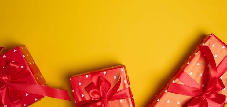 Gift box tied with a red bow on a yellow background, top view