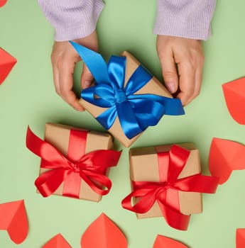Woman's hand holding a gift box wrapped in a red silk ribbon on a green background, top view