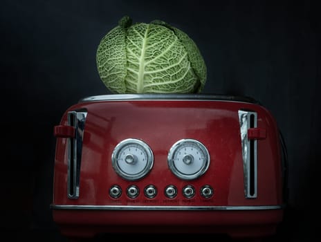 London, UK - Feb 20, 2024 - A lonely fresh savoy cabbage put on a red retro styled toaster on dark background. Whole head of organic savoy cabbage, Space for text, Selective focus.