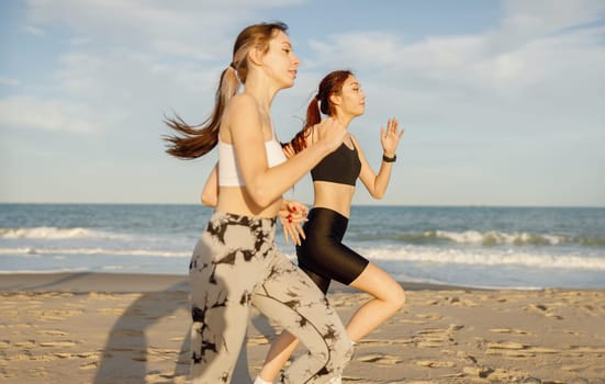 Young female friends in sportswear running on beach in morning sunrise. Outdoor workout routine