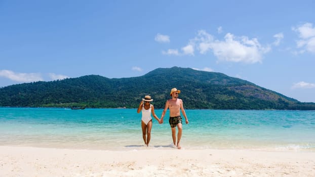 A couple of men and women on the beach of Koh Lipe Island Thailand, a tropical Island with a blue ocean, and white sand. caucasian man in a swim short and an Asian Thai woman in a bikini on the beach