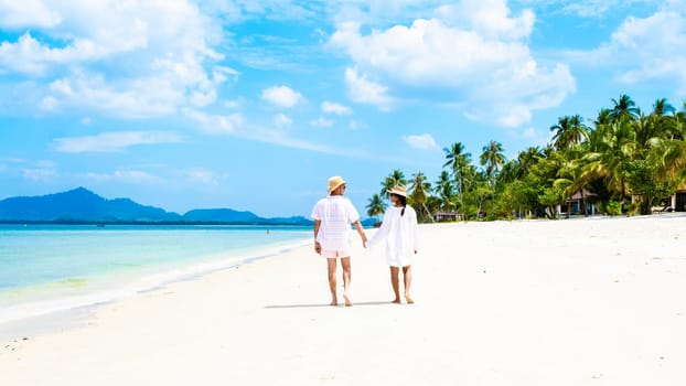 a couple of men and woman with summer Koh Muk tropical island, a caucasian man and Asian woman walking on a white beach with palm trees during summer holiday vacation in Koh Mook Trang Thailand