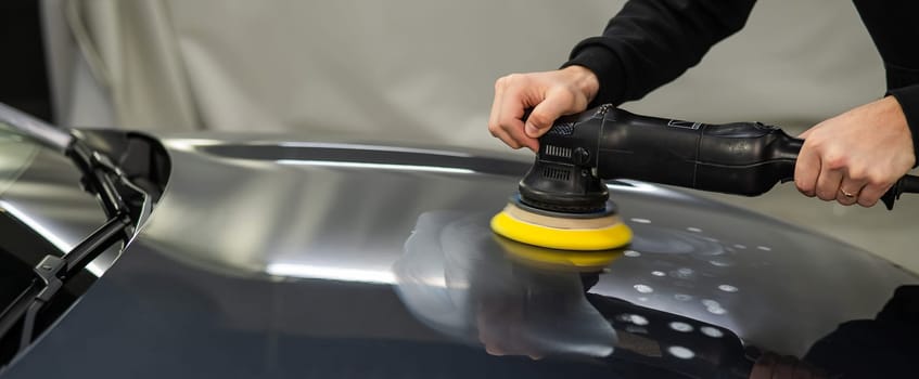 A mechanic polishes the surface of the hood of a gray car