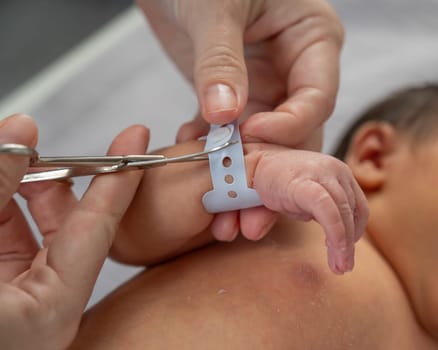 A woman cuts a tag from a newborn boy's hand with nail scissors. Close-up of hands