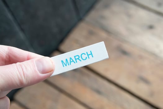 Hello March creative concept. A hand holds a sign with an inscription.