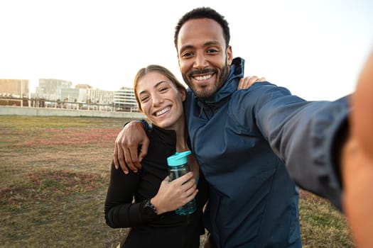 Young multiracial couple taking selfie after workout outdoors. Sporty couple taking self portrait after running in the park. Sport and technology.