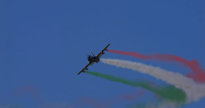 Montagnana Italy October 8 2023: Radio controlled aircraft performs against a deep blue sky, leaving a tricolor trail representing the Italian flag, with space for text. Model: Aermacchi MB-339.