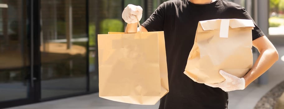 Contactless delivery during COVID-19 pandemic lockdown concept. Courier wearing mask and gloves holds a parcel box and checking address details on the smartphone.