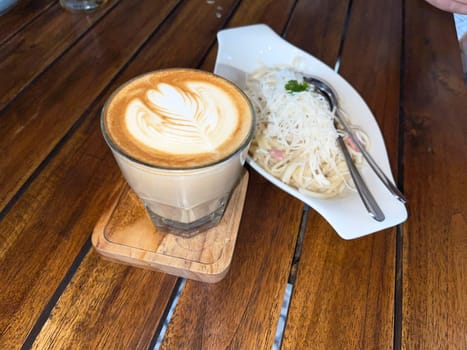beautiful cup of cappuccino coffee with latte art and spaghetti alla carbonara in white plate with wooden space background