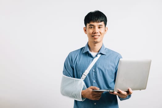 An Asian businessman, despite a broken arm, maintains confidence, using a splint for treatment while working on a laptop. Studio shot isolated on white background, emphasizing dedication and recovery.