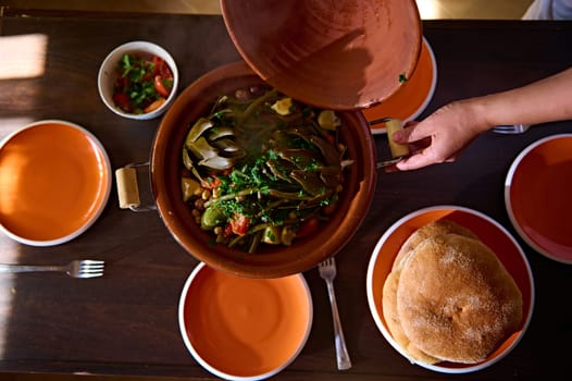 Food background with Moroccan tagine cooked at home. View from above of organic healthy vegetables, artichoke, beans, tomatoes teamed in a clay pot, cooked according to traditional Moroccan recipe