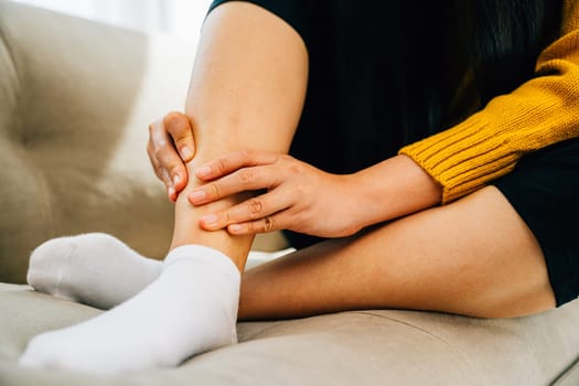 Woman seated on sofa clutching her painful ankle portraying discomfort. Reflecting health care varicose vein prevention and emphasizing leg recovery and pain relief concept. medical
