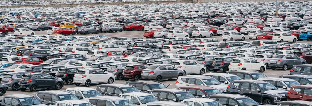 Lamchabang, Thailand - July 02, 2023 In a sunny car factory's distribution center, new hatchbacks occupy rows. The top view offers a glimpse of a crowded parking lota hub of modern business.