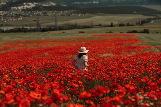 Field poppies woman. Happy woman in a white dress and hat stand with her back a blooming field of poppy. Field of blooming poppies