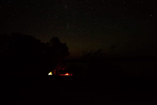 Tourists enjoying the night sky on the lake with a tent by the fire