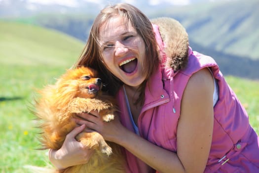 A small red dog (Pomeranian Spitz) licks a woman's face forcing her to laugh