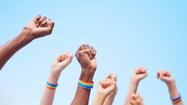 Cropped image of a multiethnic group of people raising arms with close fists wearing a lgbt bracelet, with copy space