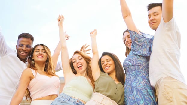 Low angle view of a happy group of friends raising the arms while smiling