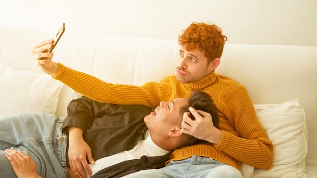 Happy gay couple taking a selfie together in the sofa at home