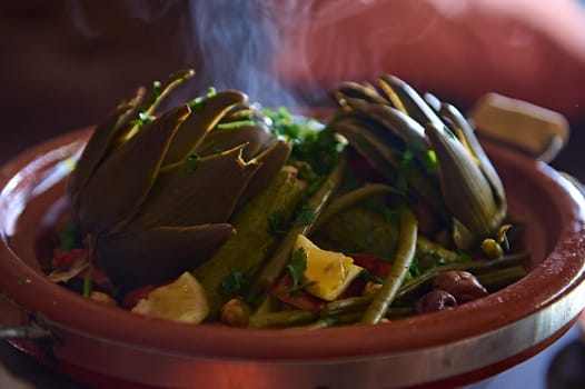 Delicious healthy vegetarian meal with steamed artichokes in tagine clay pot. Moroccan crockery, culture, cuisine and traditions. Extreme close-up photo for food blog