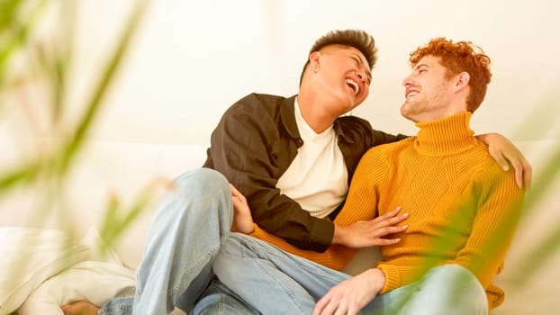 Gay couple laughing while sitting on the sofa at home